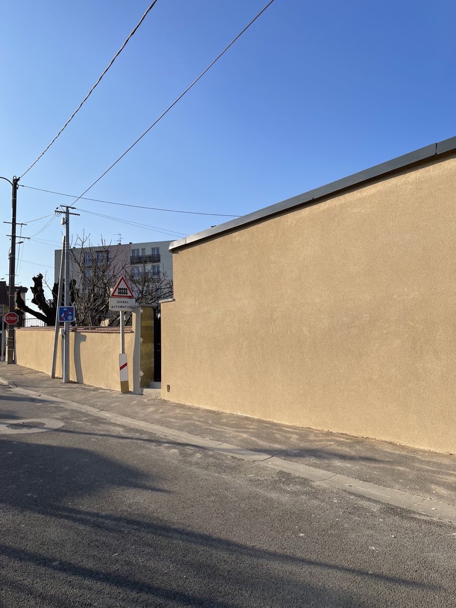 Le même mur de clôture après application d'un enduit imitation pierre beige par REIS façade