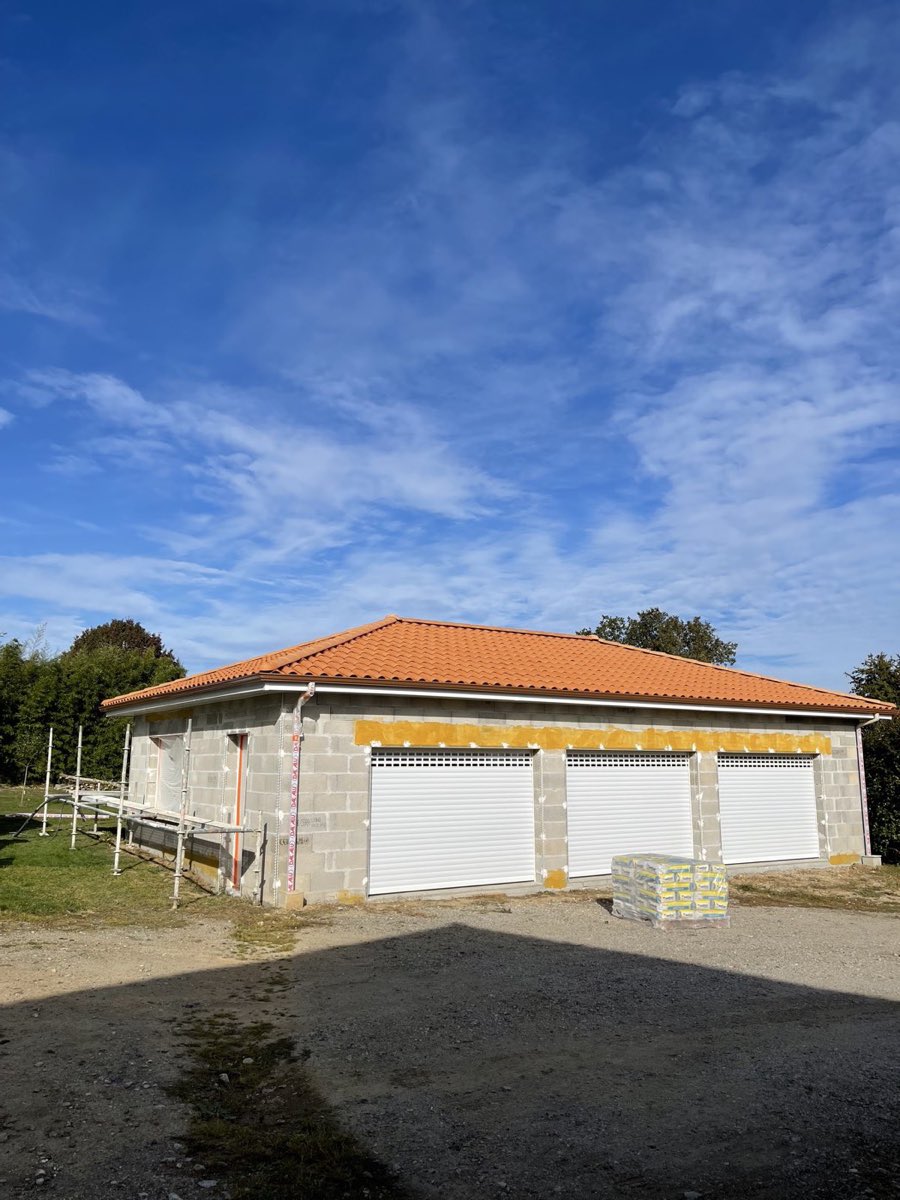 Grand garage trois portes en parpaings nus avec échafaudage, avant ravalement par REIS façade