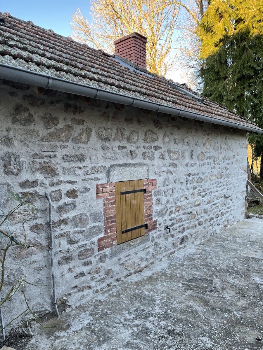 Mur en pierre apparente rejointoyé à la chaux, avec encadrement de fenêtre en brique et volet bois