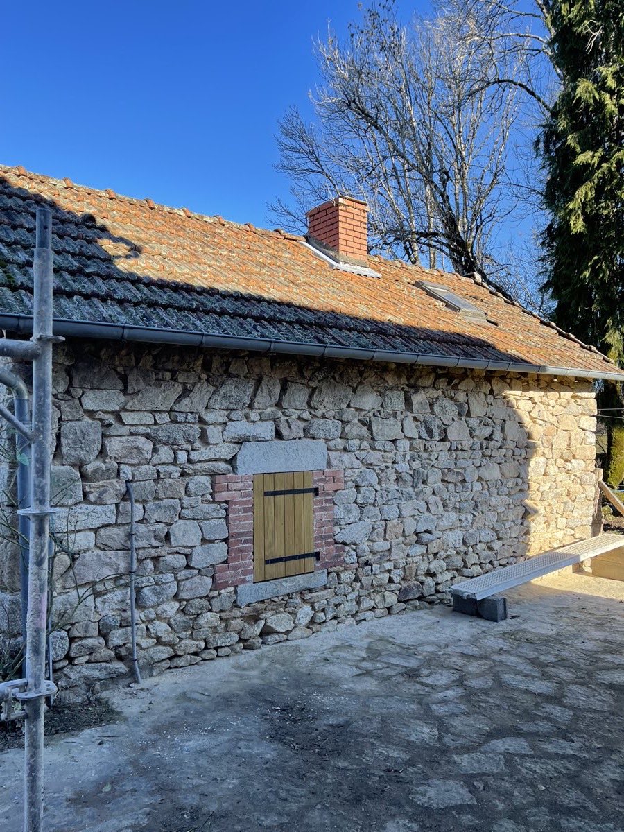 Pignon d'une grange en pierre apparente rejointoyée, sous un ciel bleu