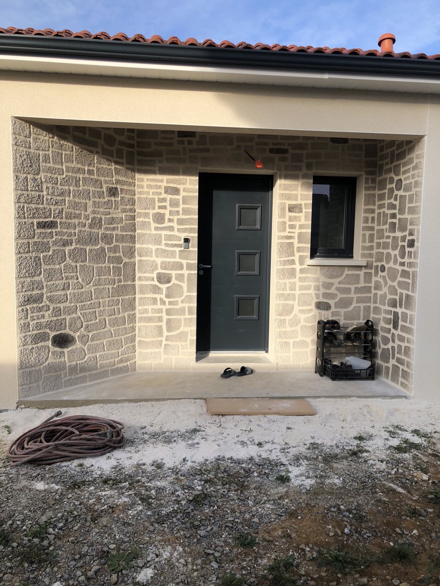 Entrée de maison entièrement habillée d'un enduit imitation pierre beige et gris, vue d'ensemble