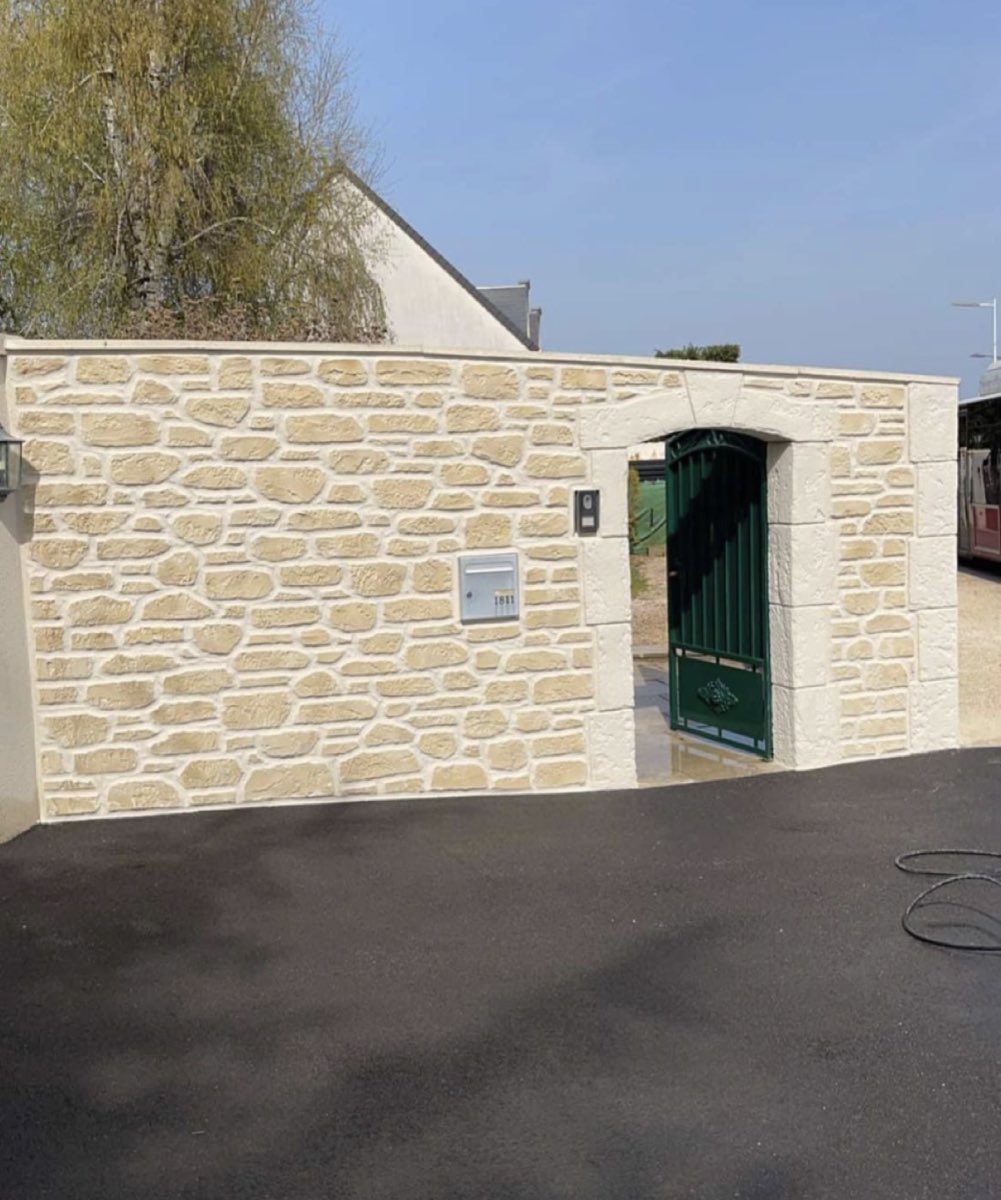 Mur de clôture en enduit imitation pierre beige avec encadrement de portail sculpté